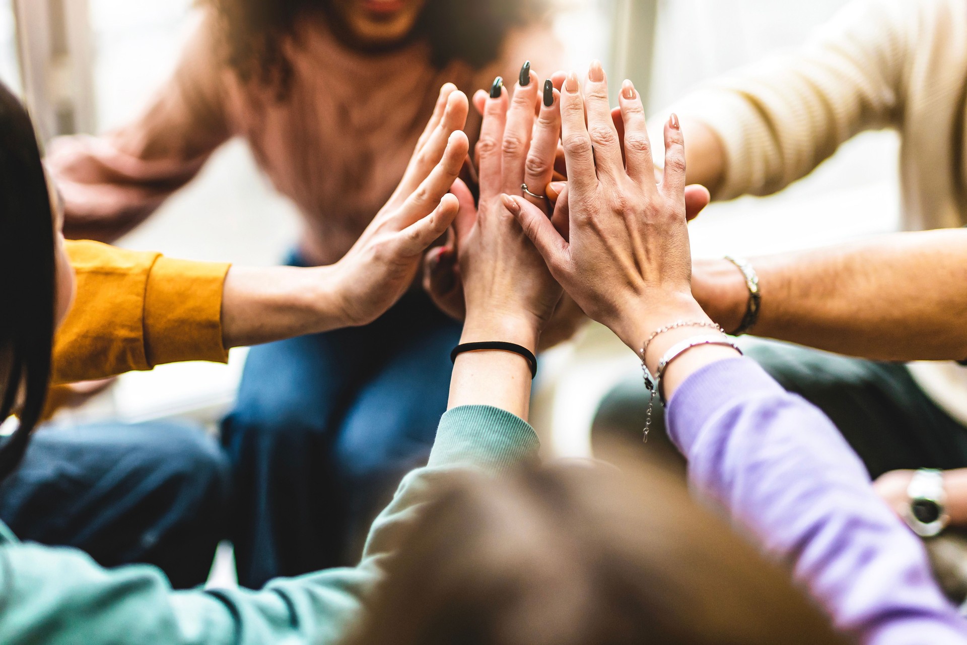 Giovane gruppo multietnico che unisce le mani – Amici diversi e felici uniti attorno a un tavolo comunitario che si divertono – giovani studenti millennial che danno forza e motivazione – concetto di lavoro di squadra e risorse umane.
